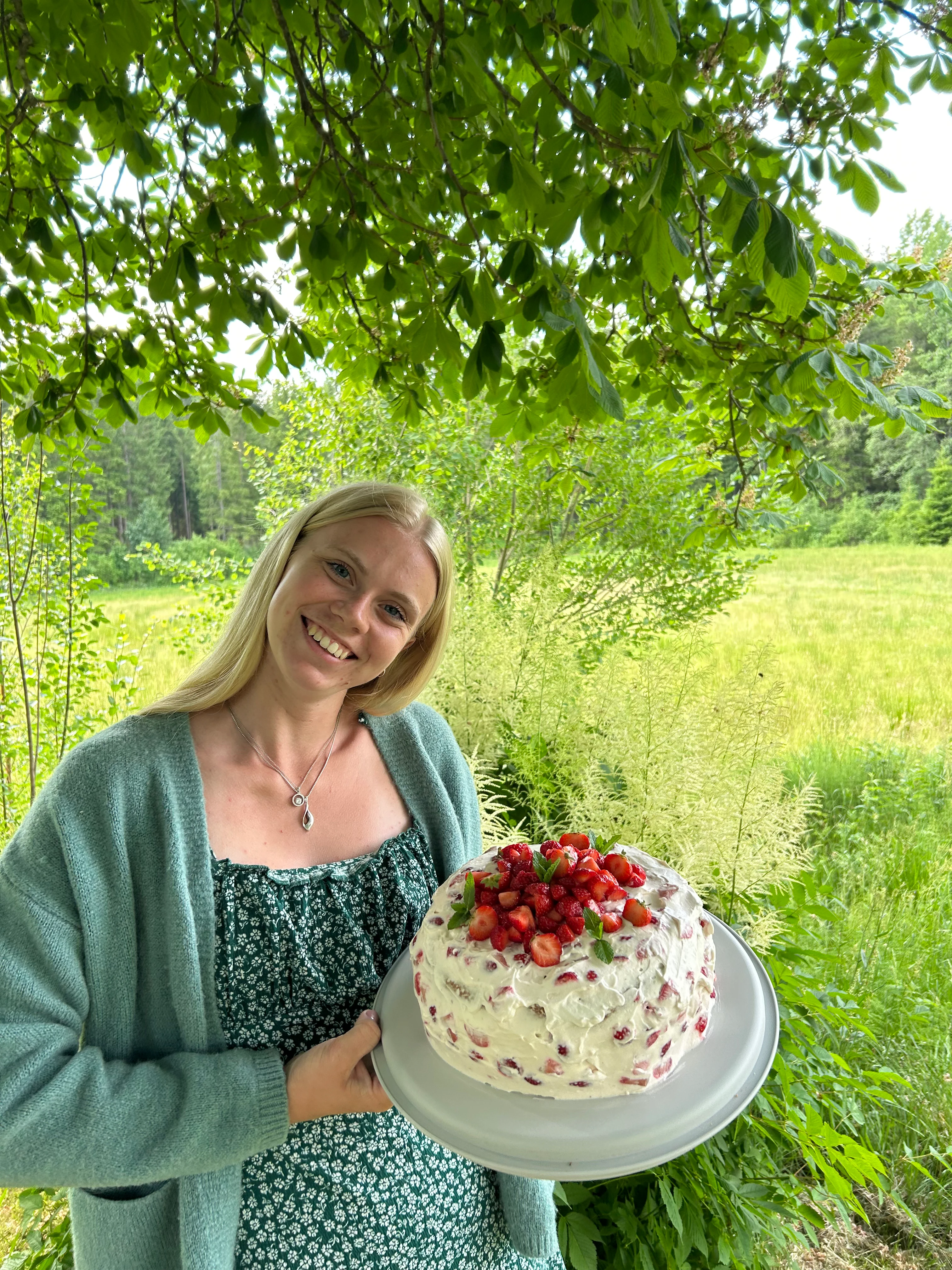 Josefine under ett träd med en rund vacker jordgubbstårta